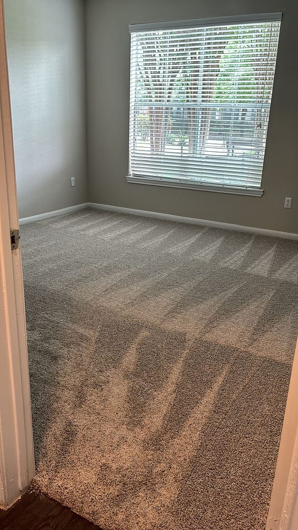 Empty bedroom with fresh vacuum lines on the carpet and clean blinds, ready for moving in.