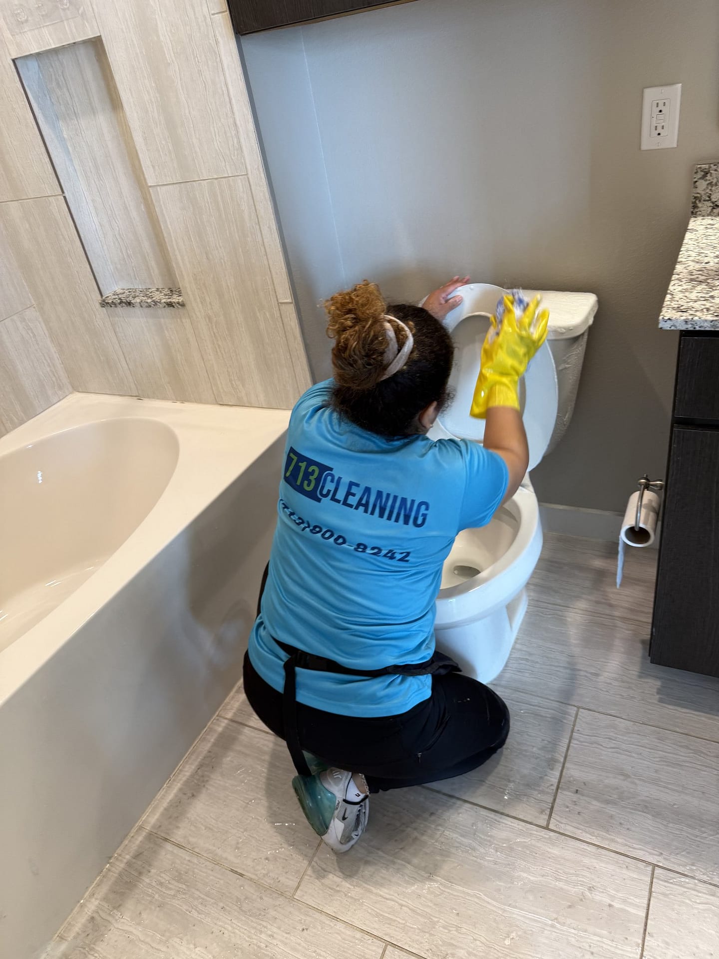 713 Cleaning team member cleaning a toilet in a Houston bathroom, where the area behind and under the base is the part most people skip.