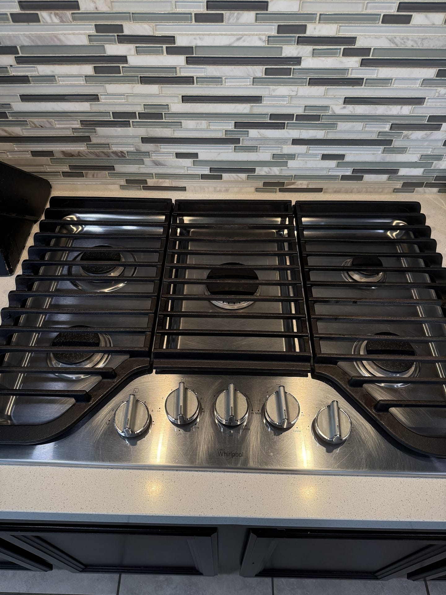 Cleaned gas cooktop with the grates back in place, the stainless control panel polished and the mosaic tile backsplash wiped down.
