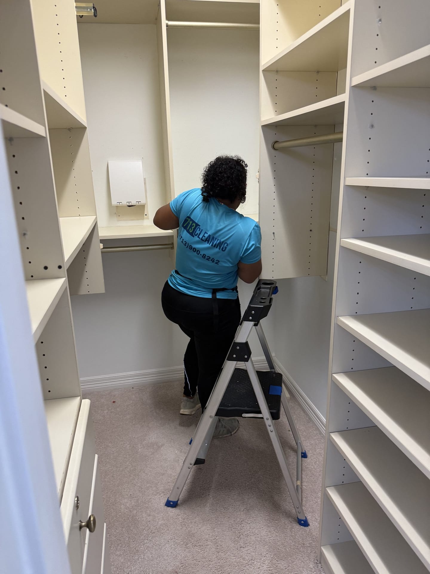 Cleaning crew member wiping the bare shelves of an empty walk-in closet during a move out cleaning.